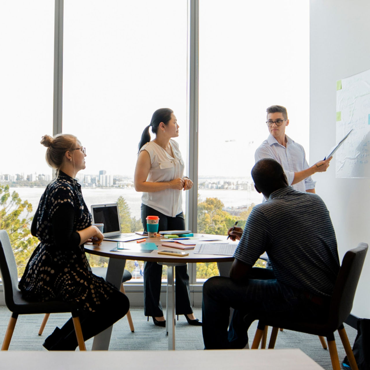 A group of colleagues in a range of races, genders, and ages are having a strategy meeting in a brightly lit office. 