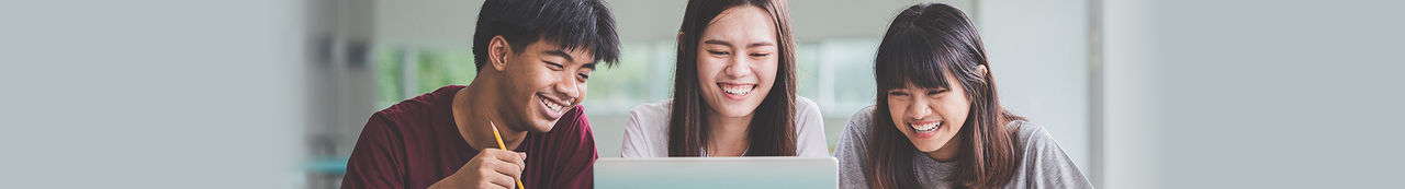 Three students sitting at desk looking at laptop and smiling